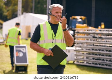 Male Production Worker With Headset Setting Up Outdoor Stage For Music Festival Or Concert