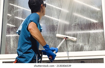 Male professional cleaning service worker in overalls cleans the windows and shop windows of a store with special equipment - Shutterstock ID 2130306539