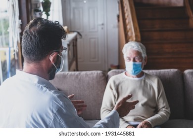 Male professional doctor consulting senior patient during medical care visit wearing masks. Young man physician and old mature senior talking providing medical assistance sitting on sofa.  - Powered by Shutterstock