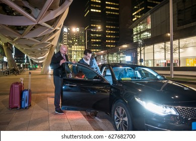 Male Professional Driver Assisting Passenger Entering Car On City Street At Night