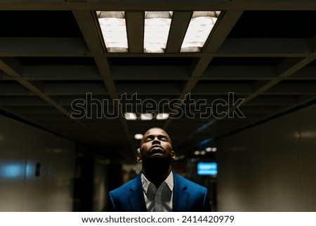 Male professional with eyes closed standing under illuminated light in subway
