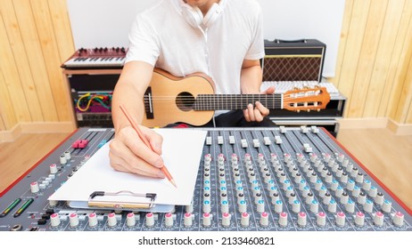 Male Professional Songwriter Enjoy Writing A Hit Song On White Paper While Playing Acoustic Guitar In Sound Studio. Songwriting Concept