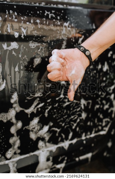 A male\
professional worker, a washerman is dissatisfied with his work,\
showing a thumbs down against the background of a black dirty\
surface of a car door and white soap\
suds.