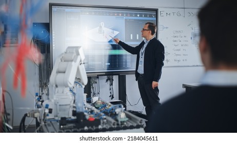 Male Professor Showing at the Big Screen During the Lesson. Diverse Group of Students Working Together on Modification of Functions of Technology Robot Arm for Engineering Project at University - Shutterstock ID 2184045611