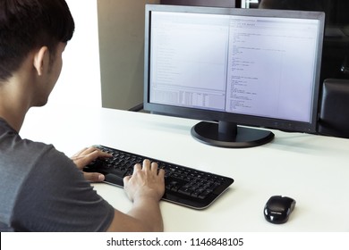 A male programmer is coding on the desktop computer with mouse and keyboard wireless on the white desk in an office.