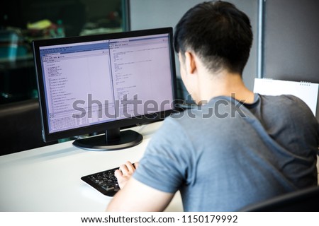 A male programmer is coding on a desktop computer on the white desk in an office.
