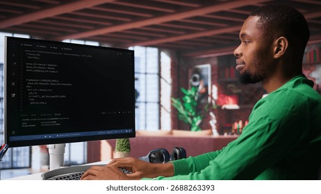 Male programmer types code on computer and running script, programming language. African american IT expert in modern loft fixing errors within the software, implementing new features. Camera A.