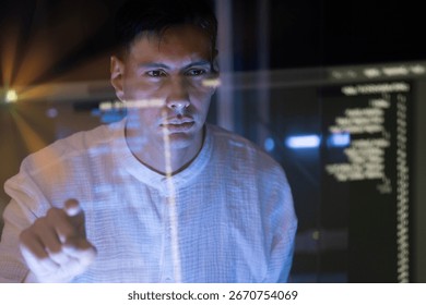 A male programmer wearing glasses is coding a hologram at night, working on data analytics, information technology, or software at the office. A futuristic technology solution for business development