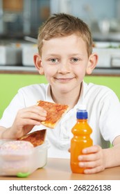 Male Pupil Sitting At Table In School Cafeteria Eating Unhealthy Packed Lunch