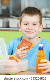 Male Pupil Sitting At Table In School Cafeteria Eating Unhealthy Packed Lunch