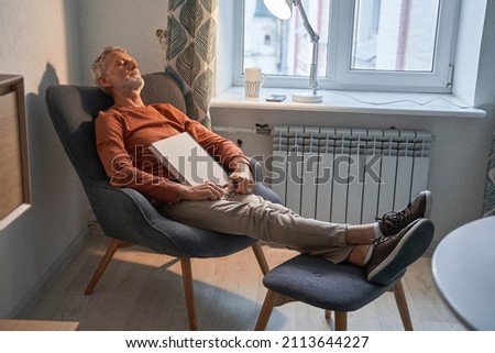 Male reader taking nap at comfortable armchair at home during the evening