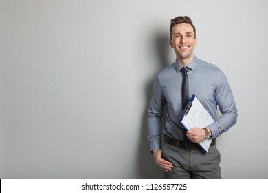 Male real estate agent with clipboard on grey background