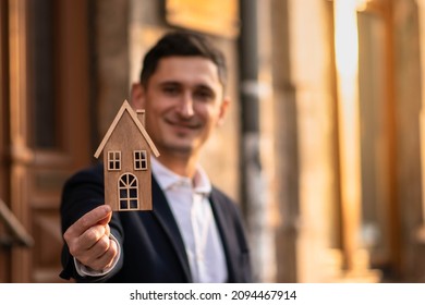 Male Realtor Standing Outside Residential Property Holding Wood House. Wood House.