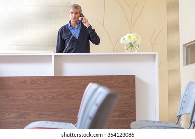 Male receptionist answering at the phone in hospital waiting room.