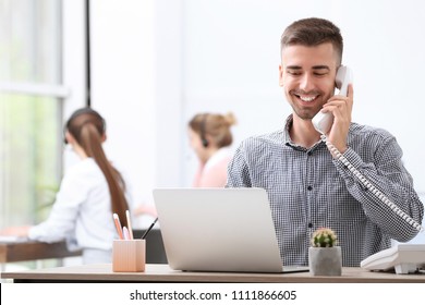 Male Receptionist Talking On Phone At Desk In Office