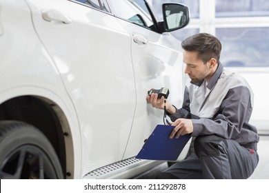 Male Repair Worker Examining Car Paint With Equipment In Repair Shop