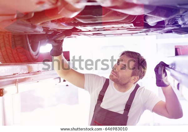 Male repair\
worker examining car in\
workshop