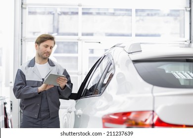 Male Repair Worker Using Tablet PC While Standing By Car In Workshop