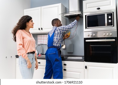 Male Repairman Checking Extractor With Digital Multimeter While Woman Standing In Kitchen