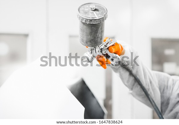 Male\
repairman painter in chamber painting automobile car elements.\
Worker paints the vehicle in white with a spray\
gun.