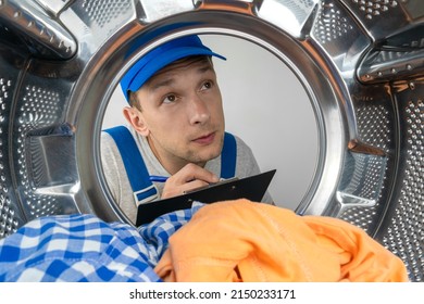 Male repairman in special clothes examines the washing machine from the inside and writes it into a paper tablet, photo from the inside. Concept of repair work