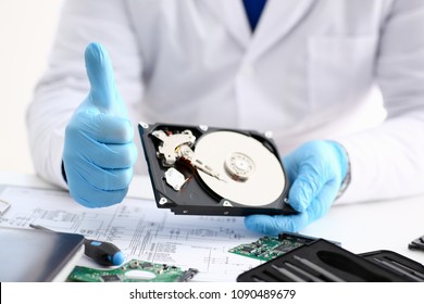 Male Repairman Wearing Blue Gloves Is Holding Hard Drive From Computer Laptop In Hands Show OK Thumbs Up. Performs Diagnostics Performs Urgent Repairs Recovery Of Lost Data During Deletion HDD Closeup