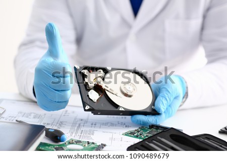 Male repairman wearing blue gloves is holding hard drive from computer laptop in hands show OK thumbs up. Performs diagnostics performs urgent repairs recovery of lost data during deletion HDD closeup
