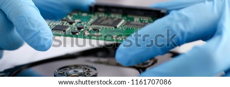 A male repairman wearing blue gloves is holding a hard drive from computer or laptop in hands. Performs fault diagnostics and performs urgent repairs recovery of lost data during deletion HDD closeup