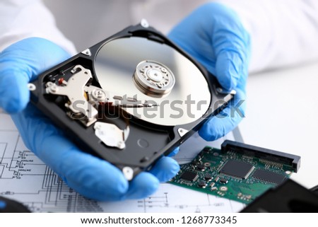 Male repairman wearing blue gloves holding hard drive from computer or laptop in hands. Performs fault diagnostics and performs urgent repairs recovery of lost data during deletion HDD closeup