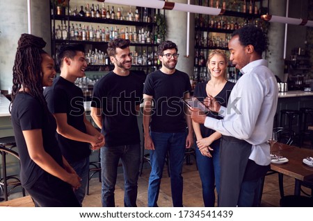 Male Restaurant Manager With Digital Tablet Giving Team Talk To Waiting Staff