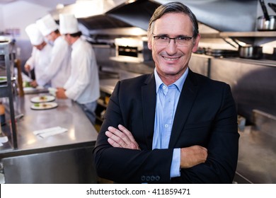 Male restaurant manager standing with arms crossed in commercial kitchen