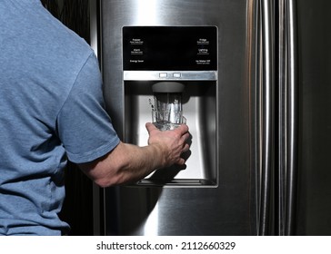 Male right hand filling glass with water splashing out of dispenser of home fridge - Shutterstock ID 2112660329