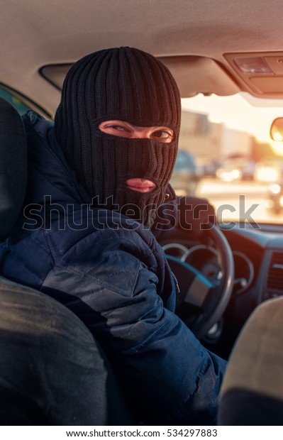 Male robber in black balaclava driving a stolen\
car, closeup