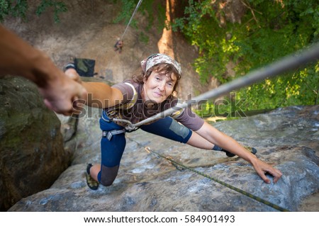 A male rockclimber is helping to old smiling female climber to reach a peak of mountain. Man giving a helping hand to the woman. View from the top