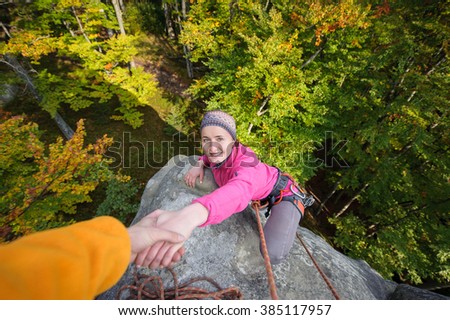 A male rockclimber is helping a young beautiful female climber to reach a peak of mountain. Man giving a hand to the woman.