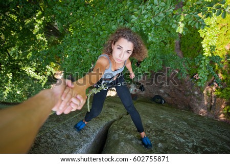 A male rockclimber is holding a young beautiful female climber on the top high of boulder. Helping hand. Climbing equipment. Top view