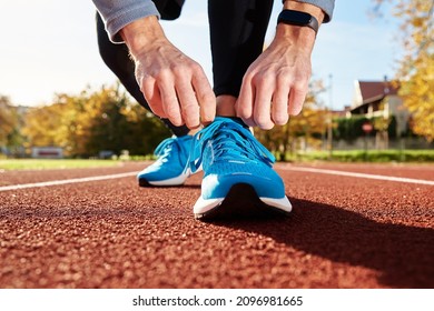 Male runner in blue sneakers get ready for run at stadium track, close up. Male hands tying on sport sneakers for jogging. Fitness and healthy lifestyle concept - Powered by Shutterstock