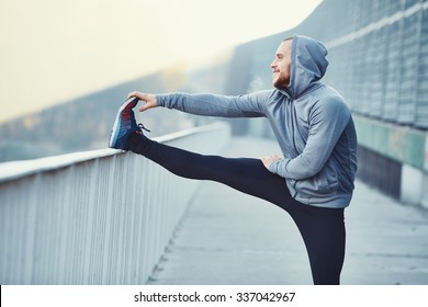 Male runner doing stretching exercise, preparing for morning workout in the park