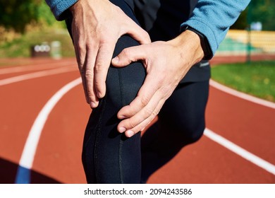 Male Runner Hands Hold On His Knee While Running At Stadium Track, Injury From Running Concept.