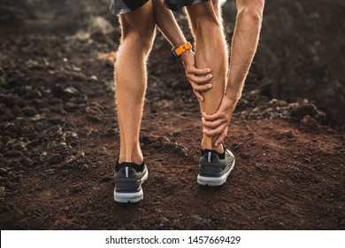Male runner holding injured calf muscle and suffering with pain. Sprain ligament while running outdoors. View from the back close-up.
