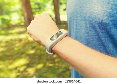 Male Runner Jogging Outside Looking At His Wearable Fitness Tracker At Sunset