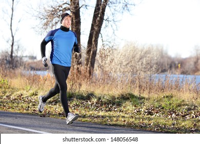 Male runner man running in autumn on cold day wearing long tights and long sporty jogging outfit. Fit male fitness athlete model training outdoor in fall. Full body length of jogger.