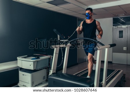 Male runner with mask running on treadmill machine testing his performance. Athlete examining his fitness in biomechanics lab.
