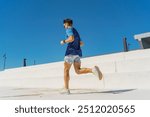 Male runner in motion on bright white steps, against a vivid blue sky, embodying energy and focus.

