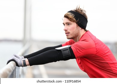 Male Runner Stretching After Running In Cold Fall Weather Wearing Warm Sporty Running Clothing. Handsome Male Fitness Sport Model Outdoors.