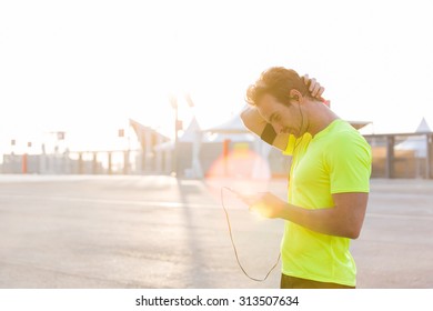 Male runner is uses a mobile phone to switch music on the play-list with copy space for text advertising, young sportsman stopped on the road after an active run while listening to music in headphones - Powered by Shutterstock