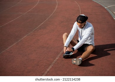 Male Runner In White Black Clothes Holds His Knee At The Stadium, Sports Injury