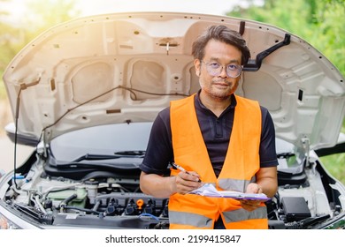 Male In Safety Uniform Standing With Check List At Car Open Front Hood. Claim Adjuster Engineer Mechanic Man Portrait Happy.