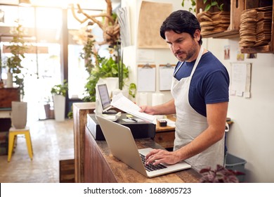 Male Sales Assistant Working On Laptop Behind Sales Desk Of Florists Store