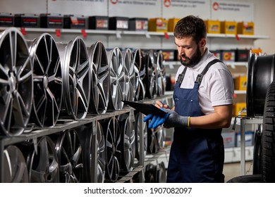 male salesman in auto shop making notes, checking the document and examining characteristics, looking at rack with auto rims - Shutterstock ID 1907082097